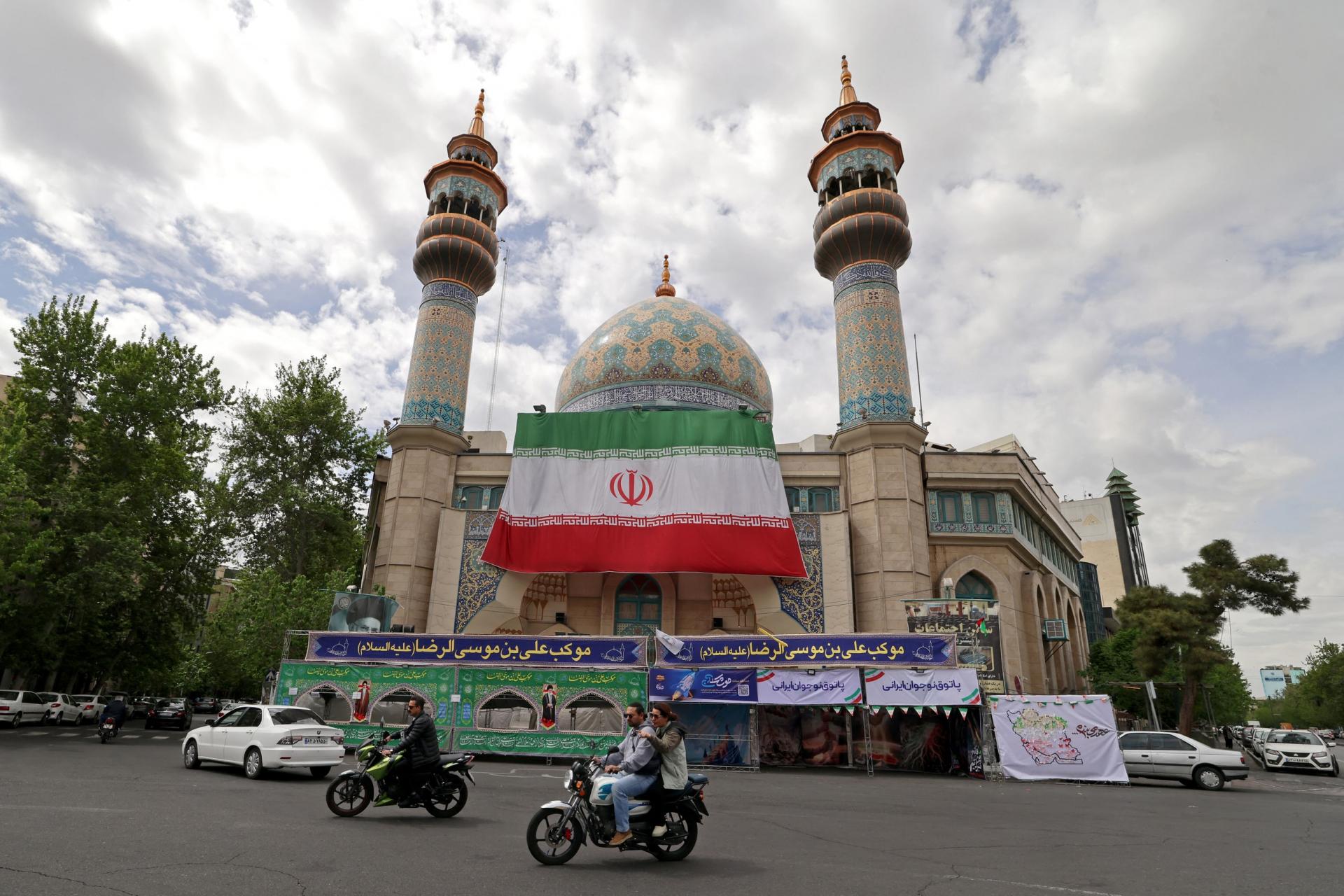 Phương tiện qua lại dưới lá quốc kỳ Iran khổng lồ treo trước nhà thờ Hồi giáo Imam Sadiq tại Quảng trường Palestine (thủ đô Tehran) ngày 19/4. Ảnh: AFP