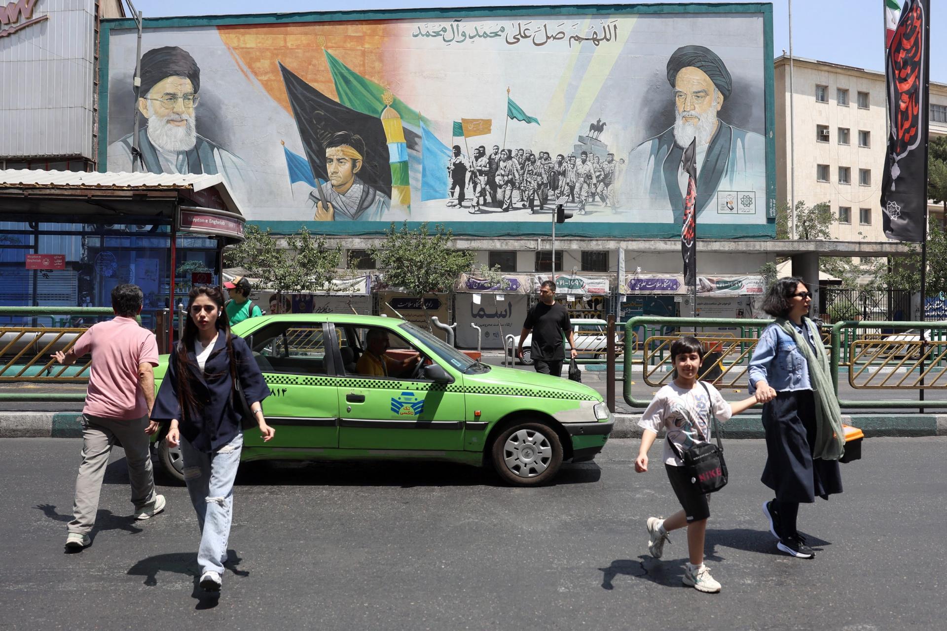 Người dân đi ngang qua bức bích họa hai cố Lãnh tụ Tối cao Iran Ali Khamenei (trái) và Ruhollah Khomeini tại thủ đô Tehran ngày 18/6. Ảnh: AFP
