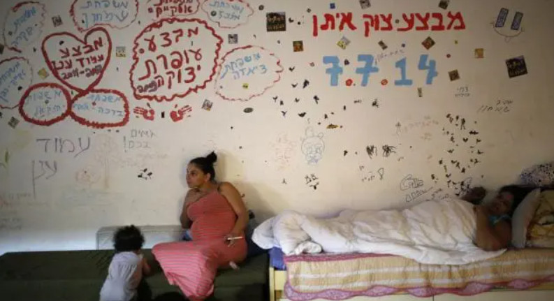 Người dân Israel trong một hầm tránh bom ở thành phố phía nam Ashkelon vào ngày 31/7/2014. Dòng chữ trên tường bằng tiếng Do Thái viết tên các gia đình và tên các chiến dịch của Israel tại Dải Gaza bao gồm: chiến dịch Cạnh bảo vệ, chiến dịch Trụ cột Phòng thủ, chiến dịch Cast Lead. Ảnh: Reuters