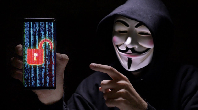Minh họa người mang mặt nạ hacker Anonymous cầm smartphone đã bị hack. Ảnh: Phonebuff/YouTube