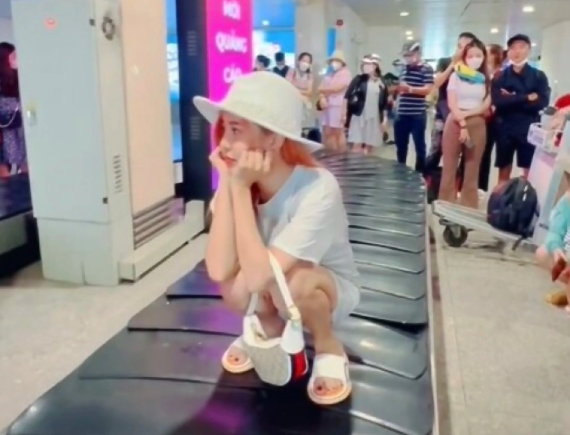 Cô gái ngồi xổm trên băng chuyền hành lý.