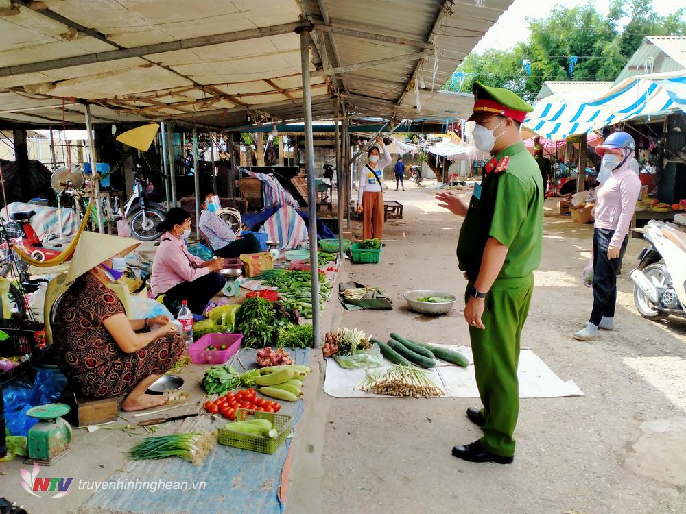 Lực lượng công an xã Quỳnh Văn nhắc nhở người dân thực hiện nghiêm thông điệp 5K trong mua bán, trao đổi hàng hóa tại chợ Vân