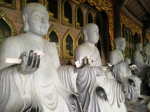 Người đi lễ đặt tiền lẻ dưới chân tượng Phật.